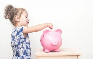 Little Girl Placing Coin In Piggy Bank.